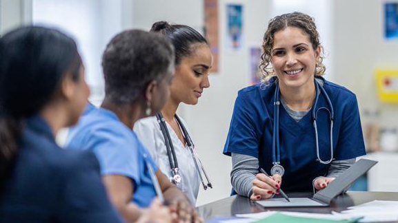 Hoitohenkilökunta keskustelemassa pöydän ääressä.