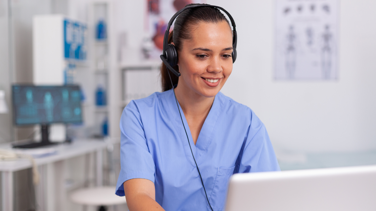 Nurse in front of a computer wearing headphones.